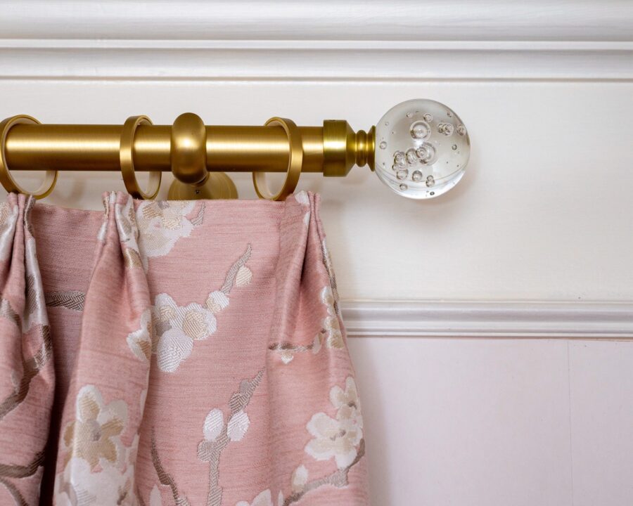 Floral patterned custom drapery hanging from a gold rod with crystal ball finials, blending sophistication and charm for an elevated interior design look.